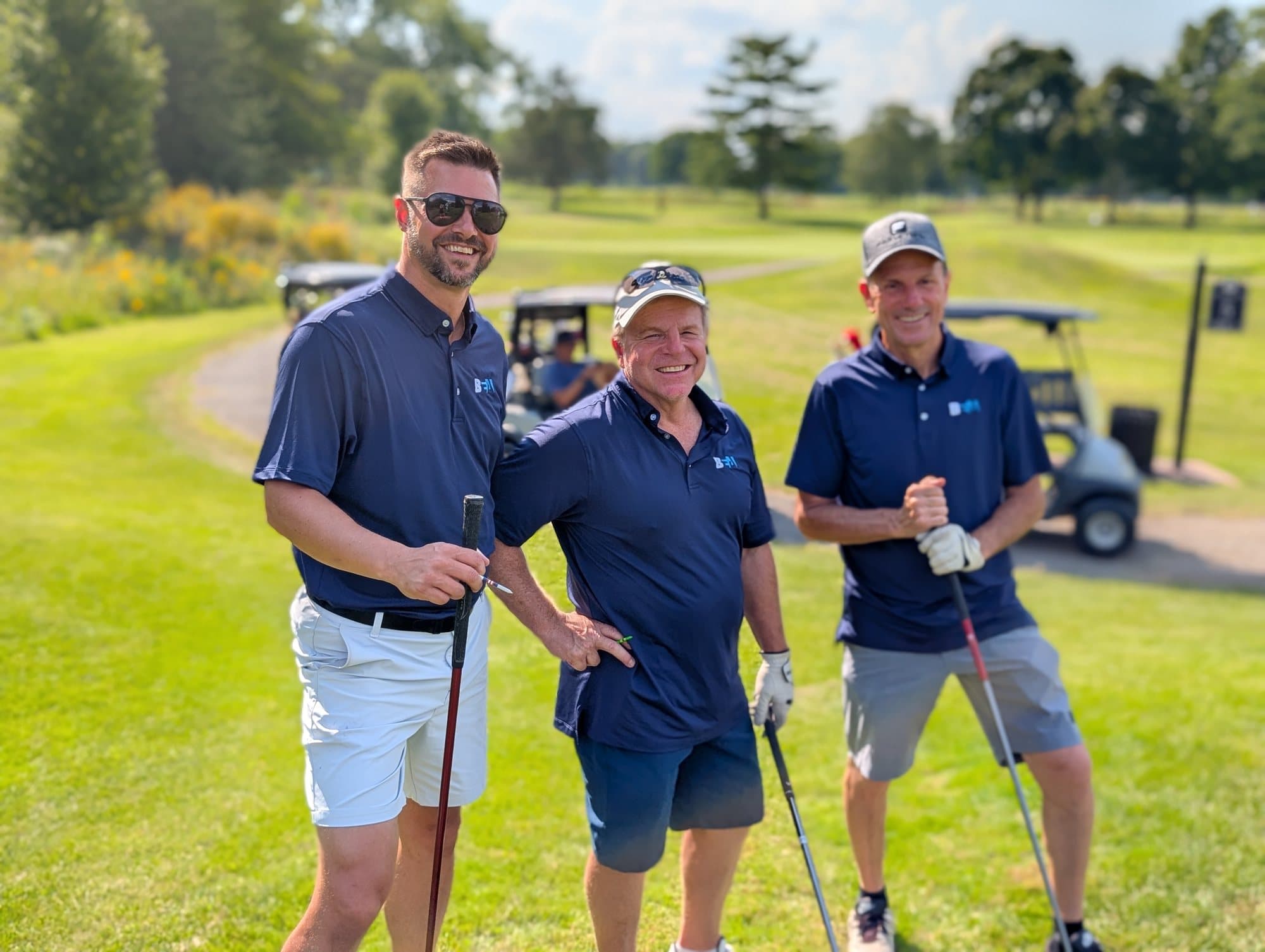 Three golfers in navy polos with the BEA logo on the chest