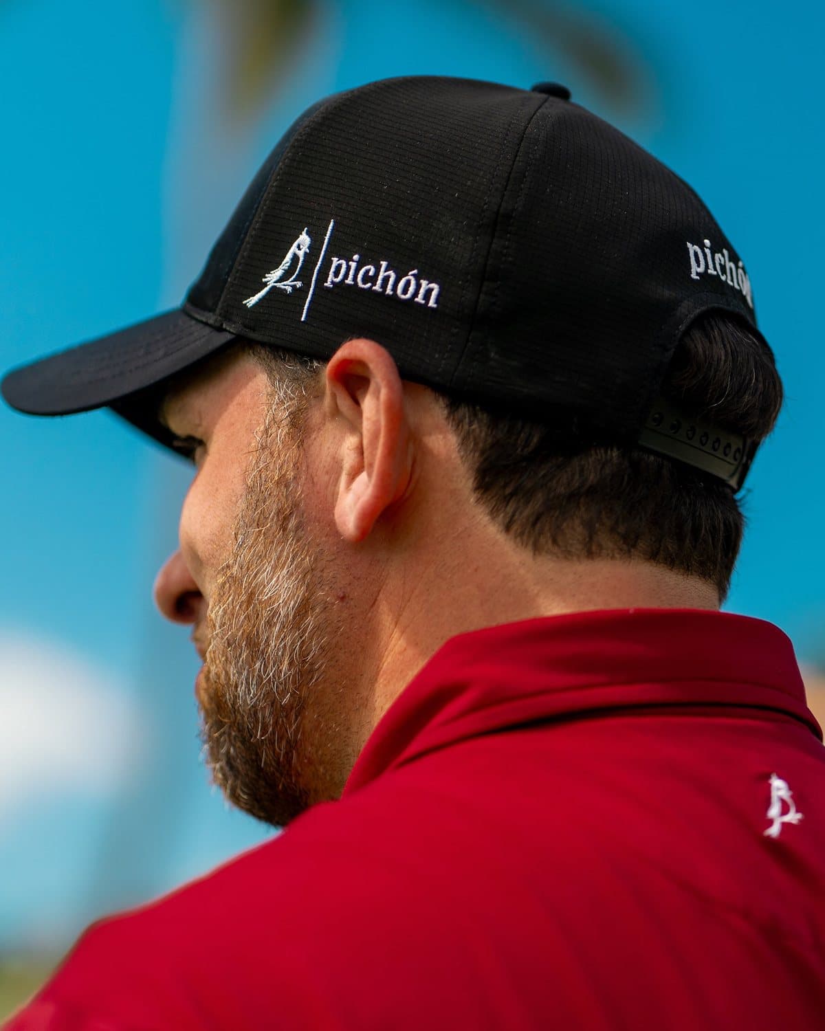A golfer wearing a black Pichón hat with an embroidered logo